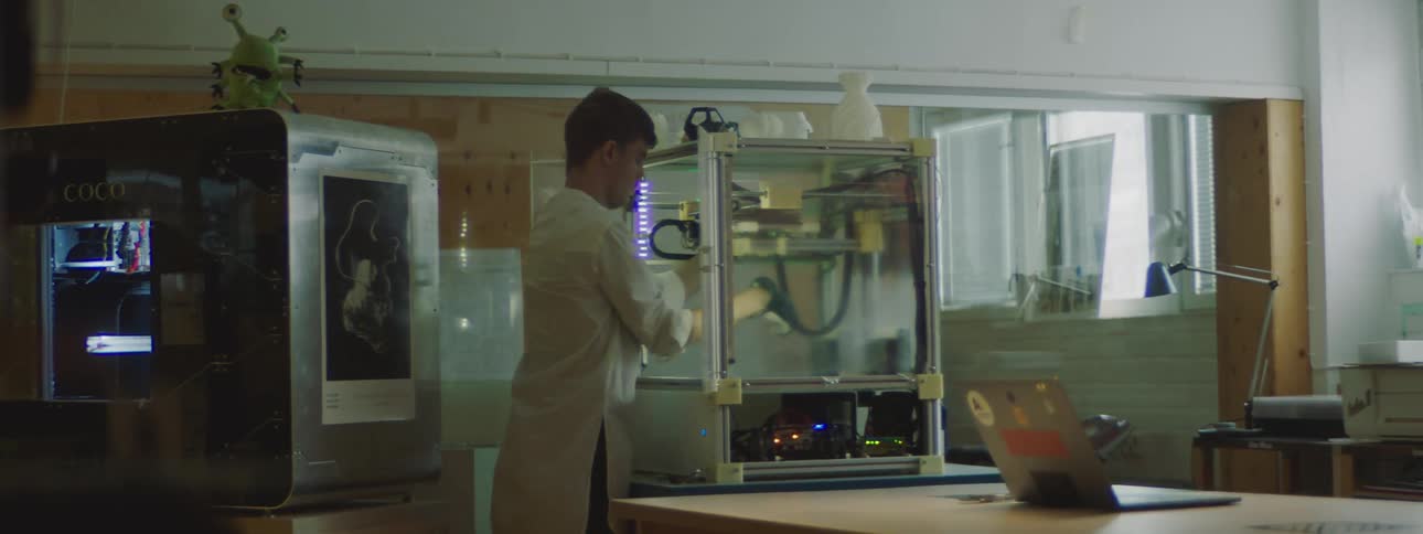A man wearing a white lab coat is working on the inside of a 3d printer