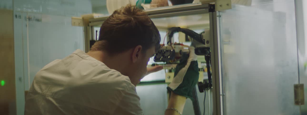 Man wearing a white shirt uses a tool to do some scraping with a gloved hand on an electronic device
