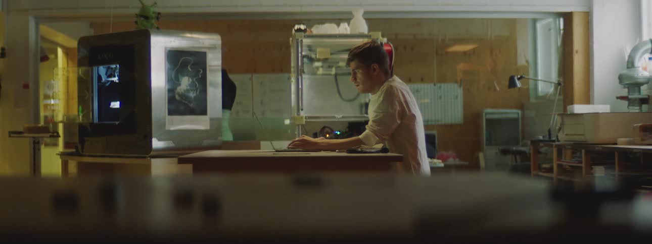 A man typing on a laptop in an office with small parts in the foreground