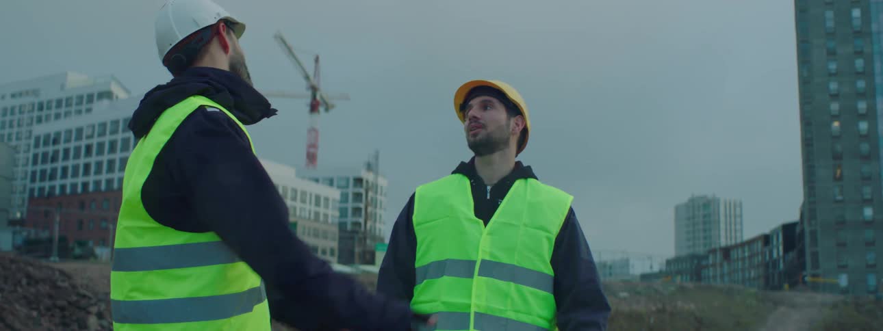 Two construction workers stand on a construction site and talk