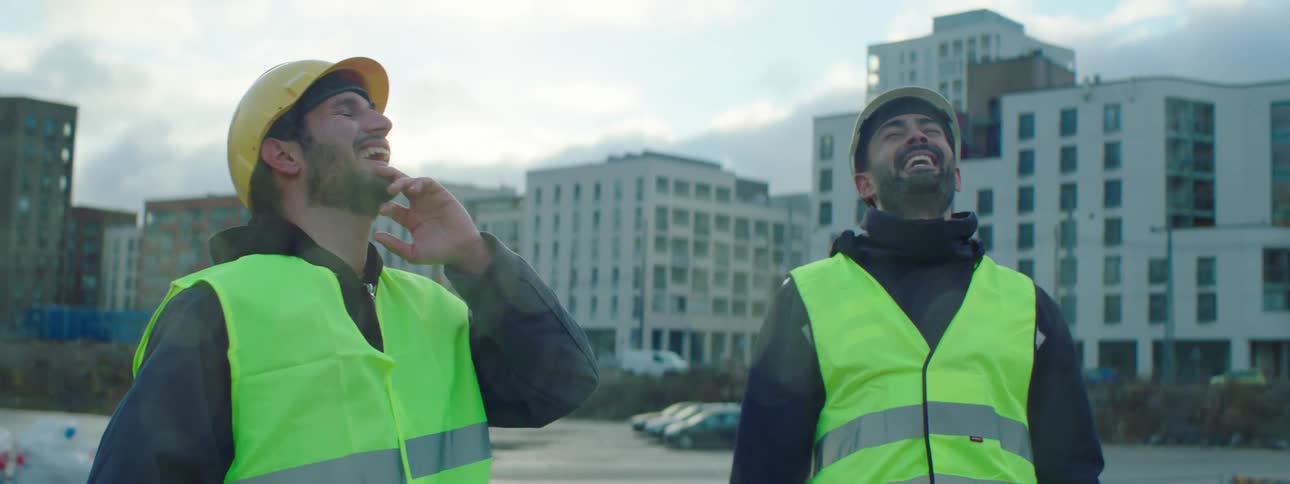 Two constructions workers talk and laugh together on the job