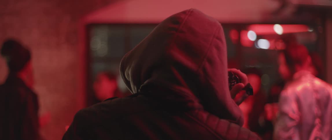 A hooded man is facing a crowd of people holding a camera