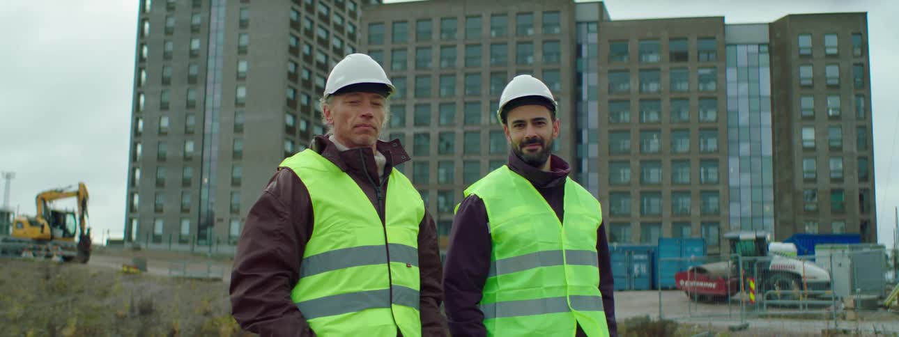 Two construction workers are standing by eachother outdoors