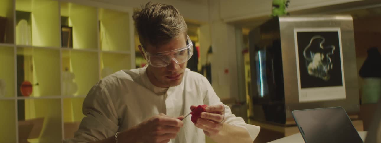 A lab worker uses a knife to carve a small red object