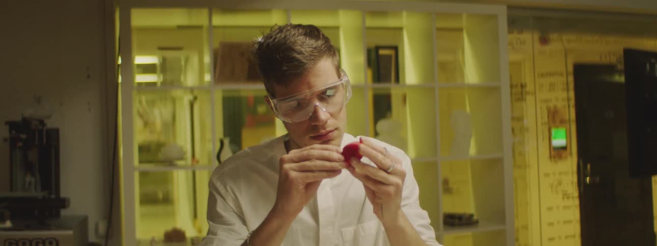 Young man wearing protective goggles peeling the skin of a red fruit in a laboratory