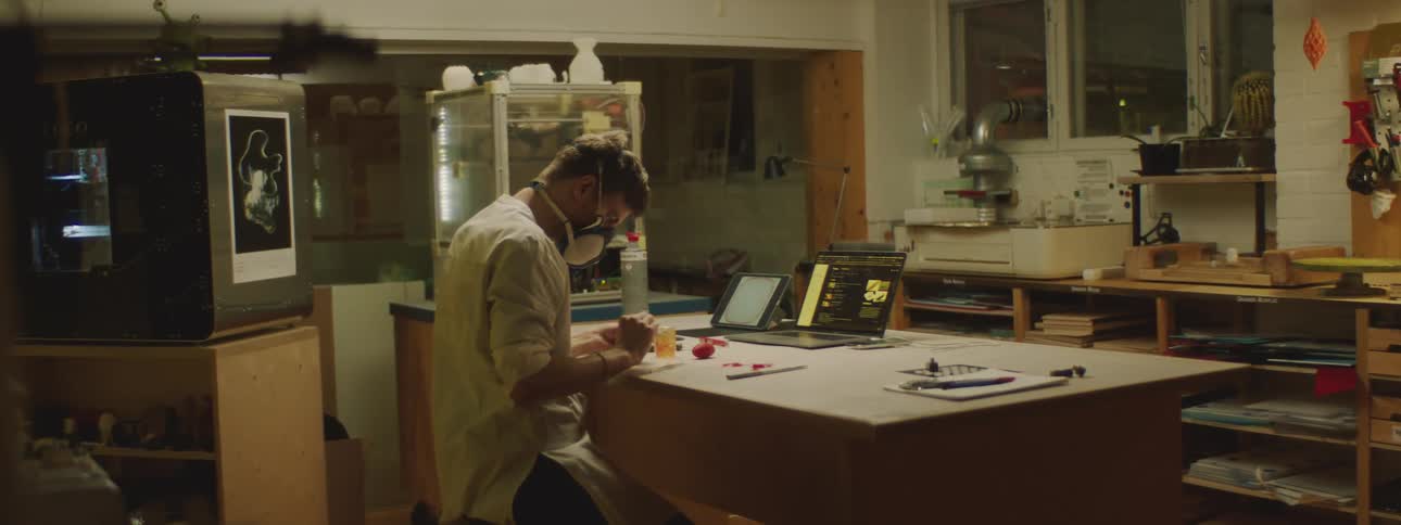 A man in a lab sits in front of laptop and works with his hands