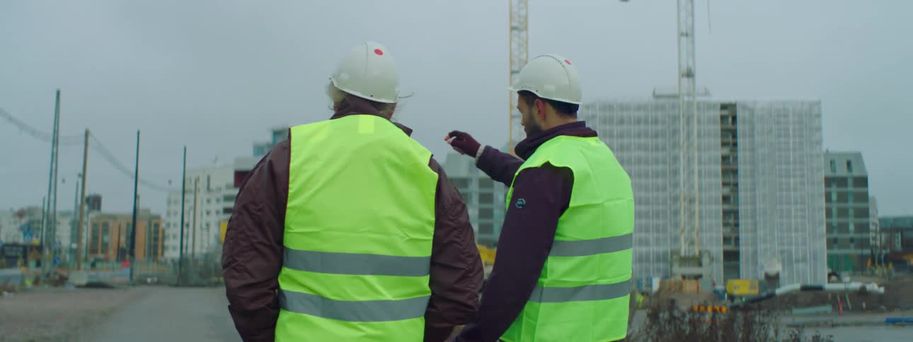 Two construction workers walk together as one points at a building as he talks