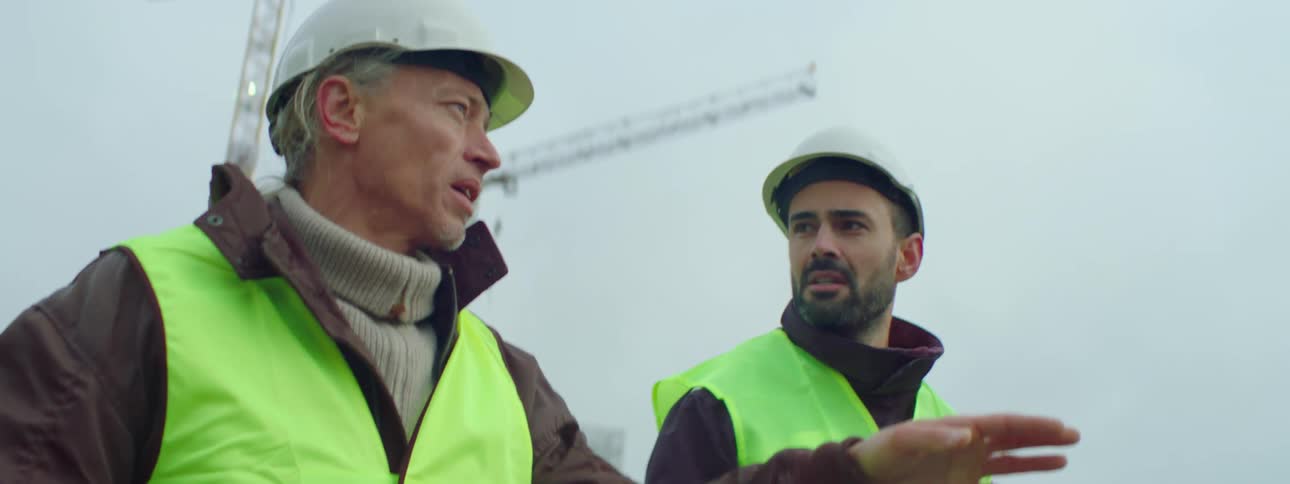 Two construction workers chat as they walk along a job site