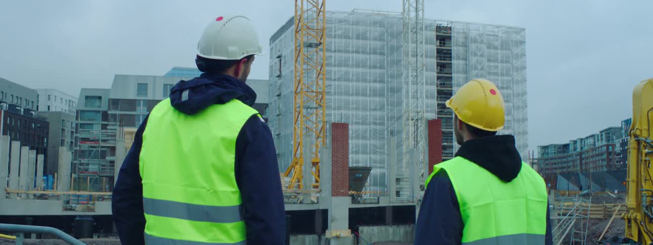 Two construction workers point as they look towards the construction site