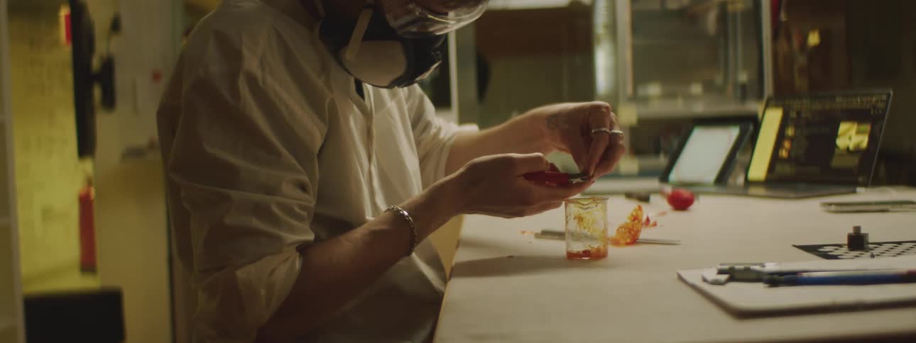 A lab worker uses scissors to trim an object into small pieces filling a beaker