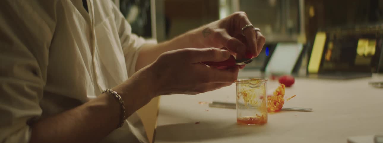 A man cutting smalls pieces of fruit with pliers on a beaker in a laboratory