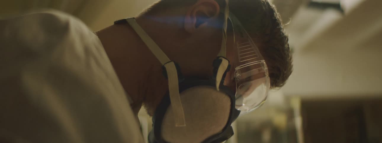 Man wearing safety glasses and a mask with straps concentrates as he works