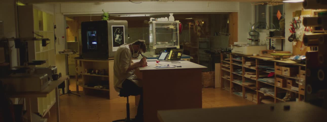 A man sitting at a counter in a lab wearing mask and goggles working with tools