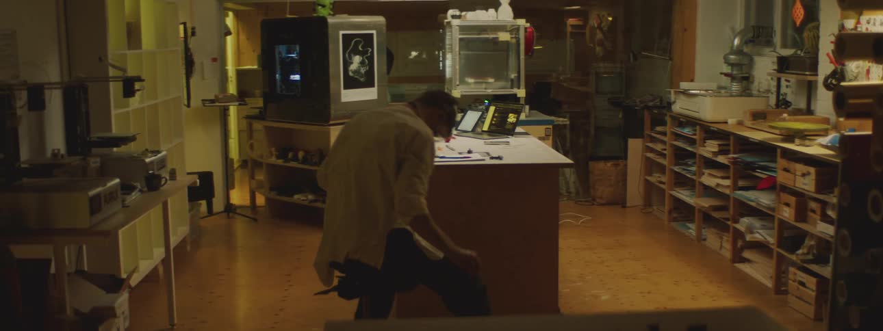 A man in a lab wheels his chair away from his desk and picks something up off the floor