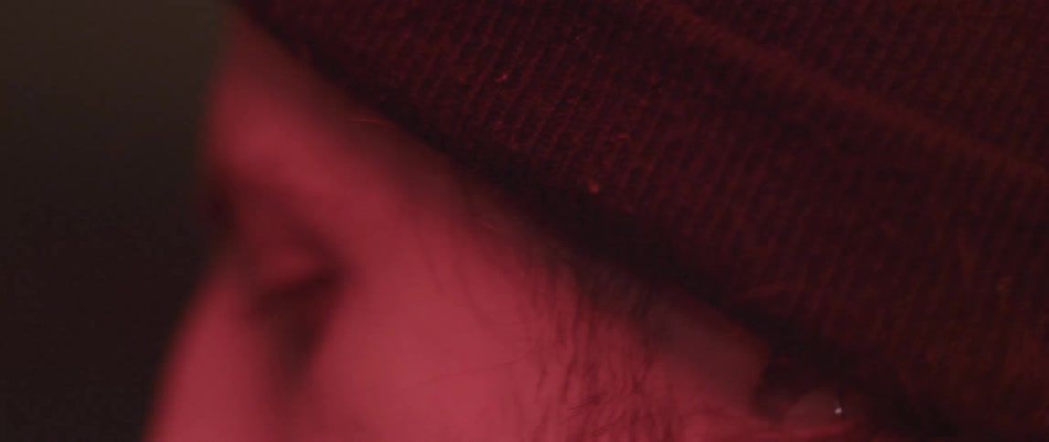 A man, who is bathed in red light, bobs his head a bit and looks back and forth
