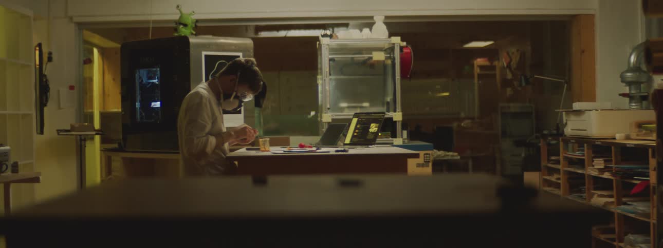 A man sitting at a table in a lab wearing a mask and safety glasses while he works