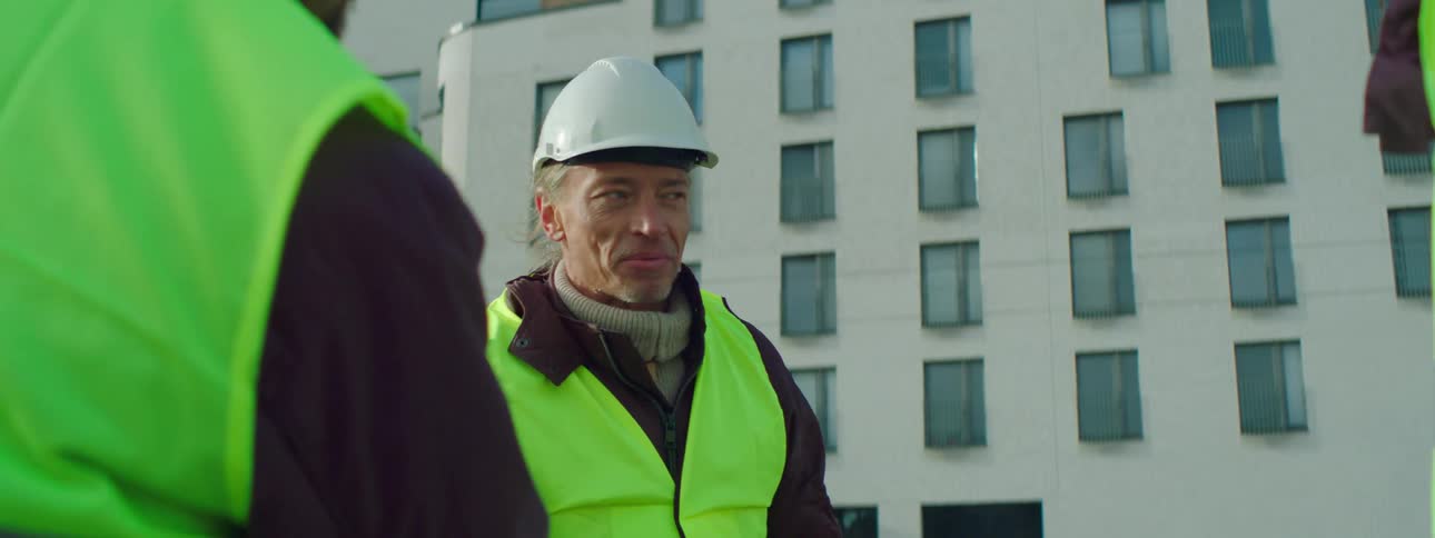 Construction workers chat and shake hands at a work site