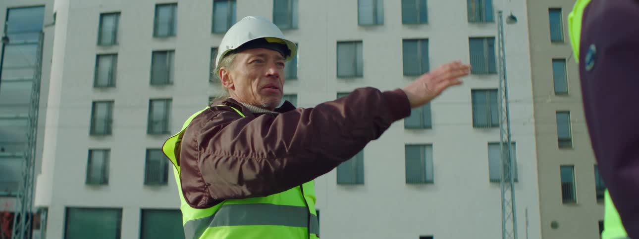 Older male construction worker gestures while talking to another worker