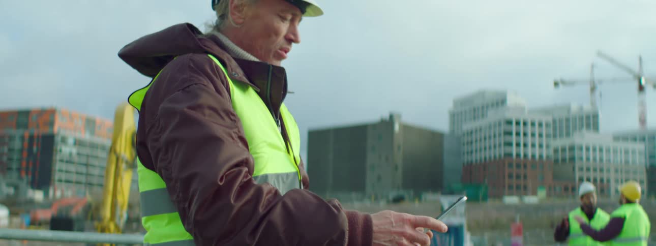 Construction worker holds a tablet as two more construction workers stand nearby