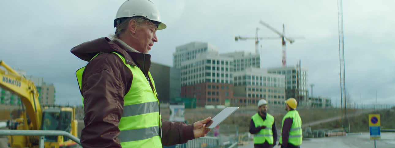 A construction worker holds a tablet having a video call on a job site