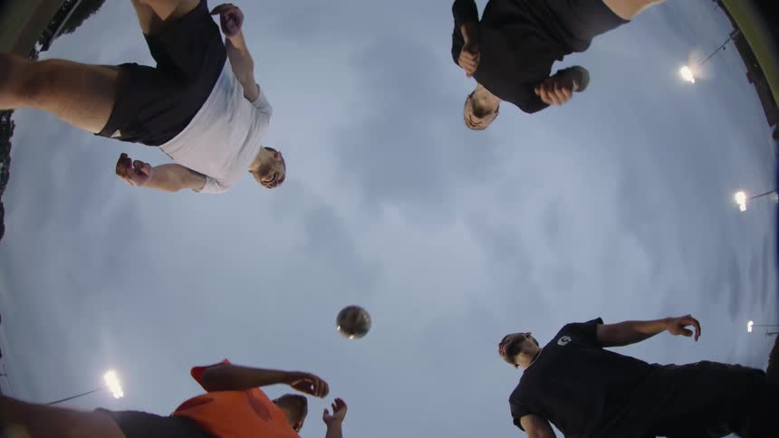 Four friends practice heading a soccer ball standing in a circle at a stadium