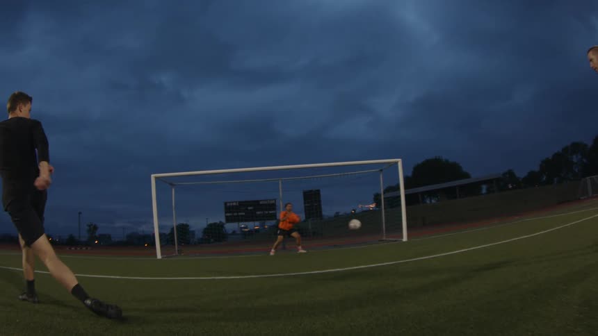 A man tosses a soccer ball into the air and a player kicks it into the goal