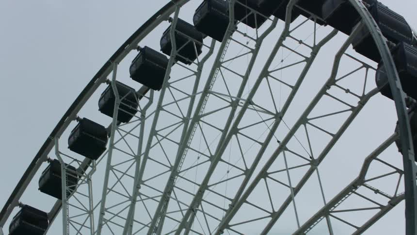 A ferris wheel in an amusement park reaches high in a cloudy sky