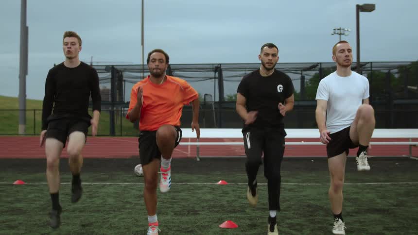 A group of men perform exercises together outdoors on a cloudy day
