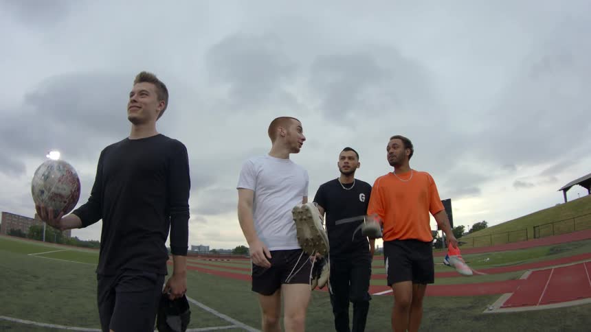Four men carry their cleats as they walk out of a soccer stadium