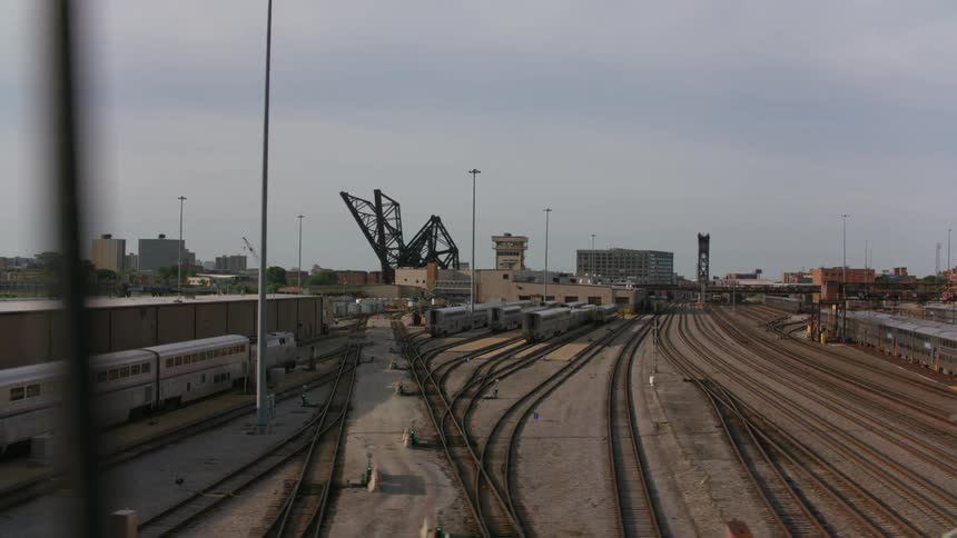 Trains are on the tracks near a train station and tall city buildings are in the distance