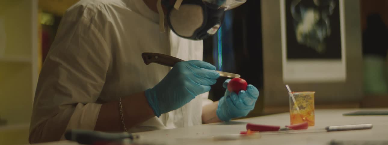 A man in a lab carefully wipes a substance on an object as he wears a mask and goggles