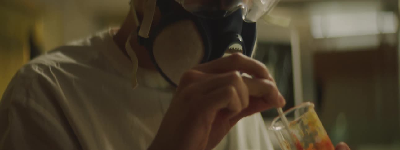 A man wearing safety glasses and air filtration mask mixing an orange fruit paste with inside a beaker in a laboratory