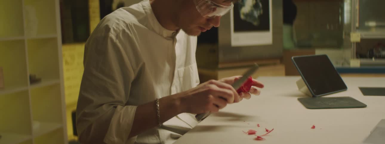 A man sitting at a table in a lab using a spatula to smooth and remove parts of a 3d print