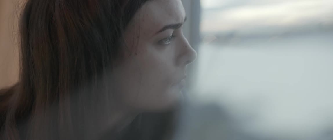 A brown haired woman looks out of a window