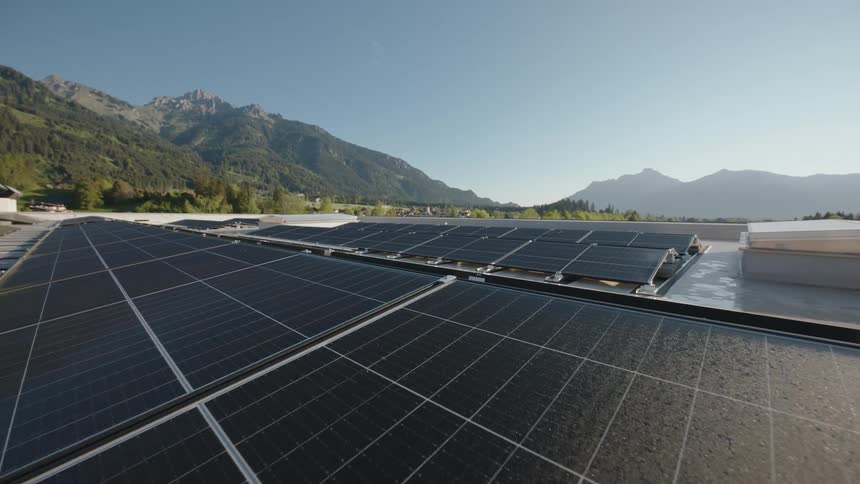 Solar panels are on the roof of a building and mountains are in the distance