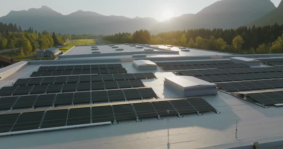 The sun shines over mountains on to solar panels on the roof of a building