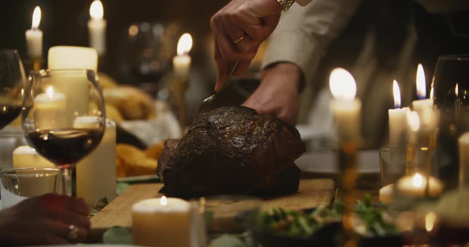 A man's hands are shown carving a piece of meat at a candle lit dinner table