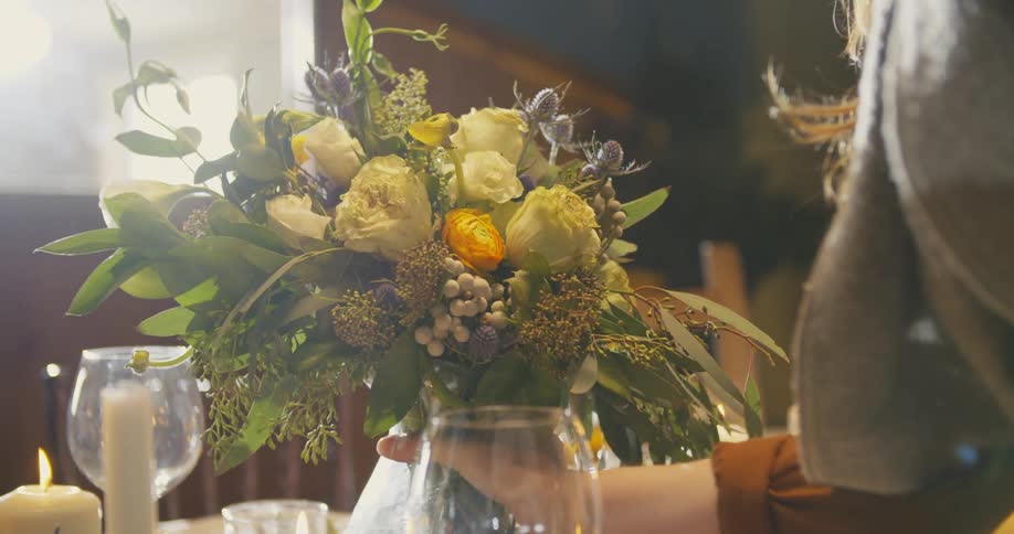 A woman places a vase of fresh flowers on a dining table