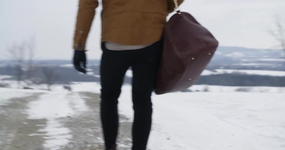 A person walks down a snow covered road carrying a bag