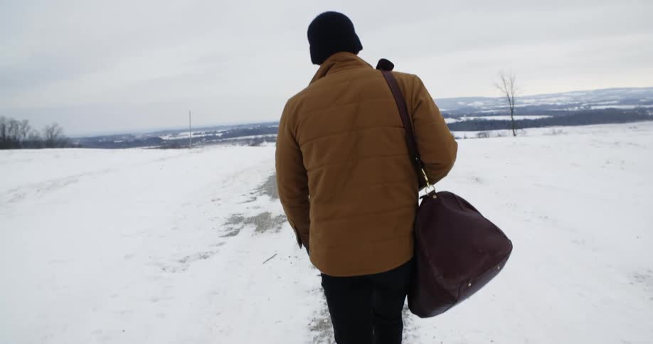 A man walks down a snowy country road in winter