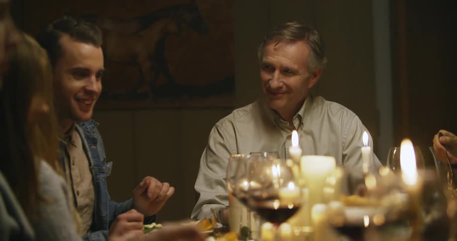 An older man looks fondly at a younger man at a family dinner gathering