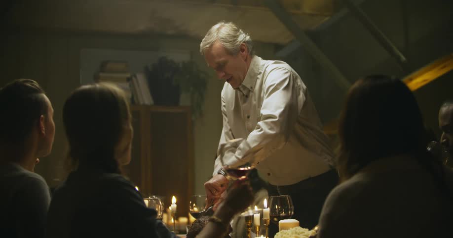 A man is cutting a roast on a table as a women drinks