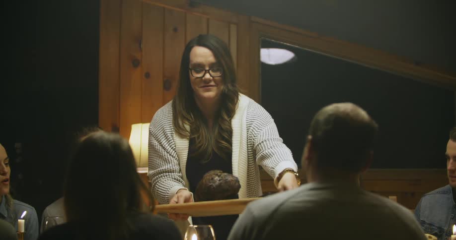 A woman sets a platter of meat onto a dining room table