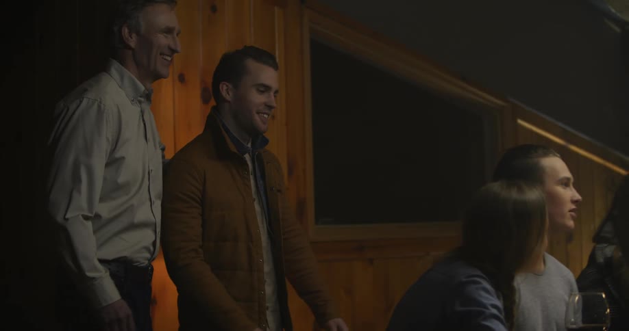 Two people enter a dining room and one man is greeted by everyone