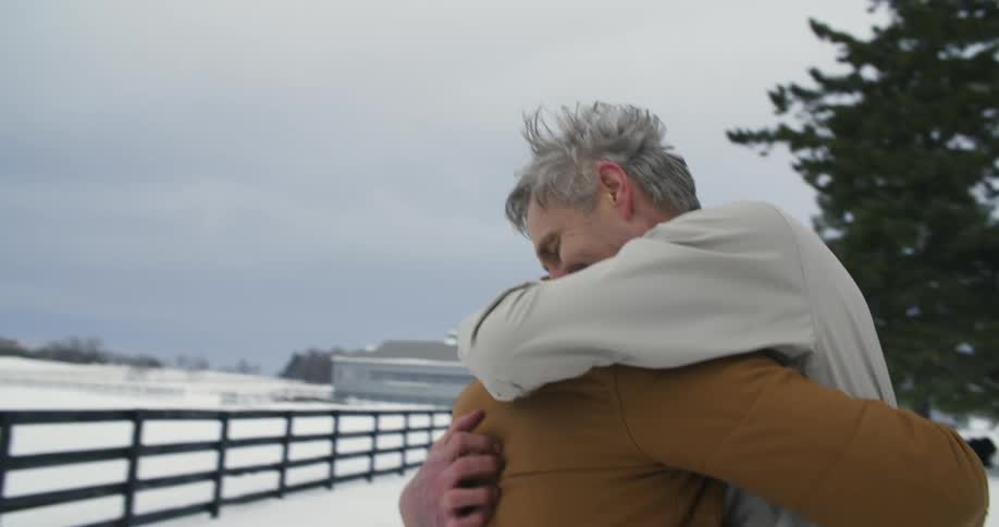 Two people are hugging near a snow covered field
