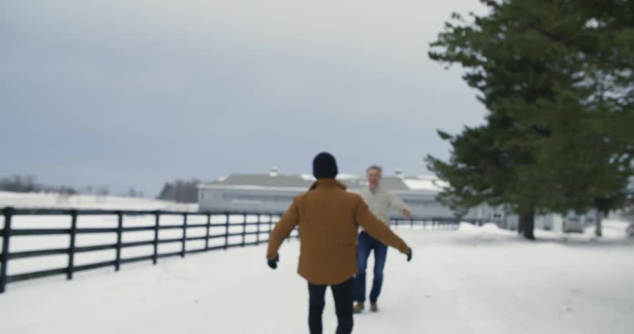 Two men run down a snowy road and embrace in a hug
