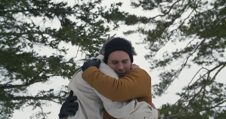 Two people hug with some tree branches blowing behind them