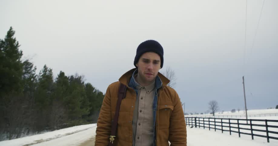 A dejected looking man walks along a street in a snow-covered rural area
