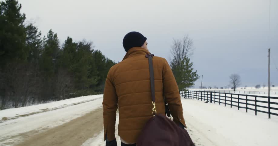 A man walking along a snowy, rural road