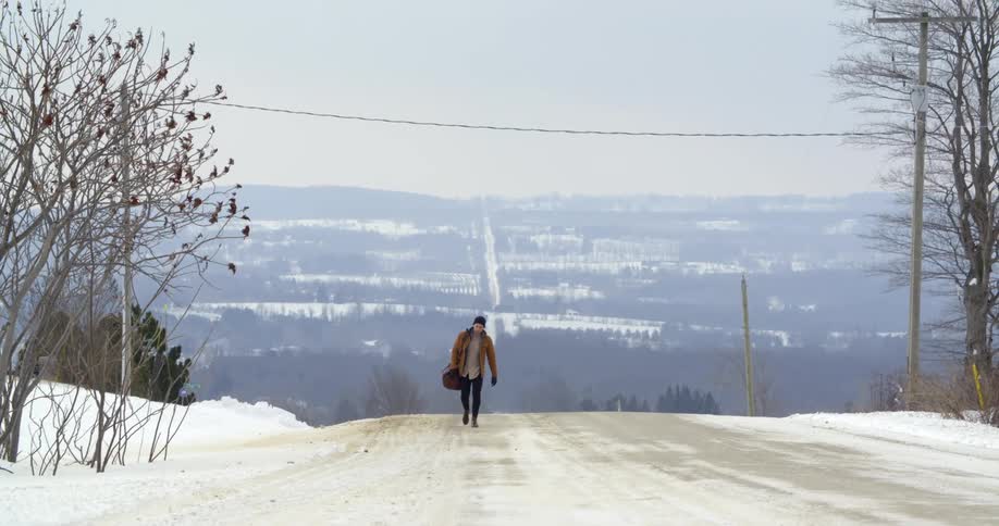 A man walks down a country road in winter